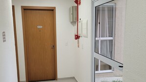 En hall med en dörr av trä, en brandlarm, ett fönster med utsikt och en svart matta vid ingången.