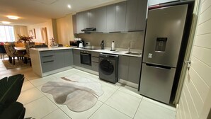 A modern kitchen with grey cabinets, a built-in washing machine, a stainless steel refrigerator, and a dining area with a table and chairs. - Cape Town Urban Elegance on Long Street | Unbeatable Table Mountain View’s (Cape Town)