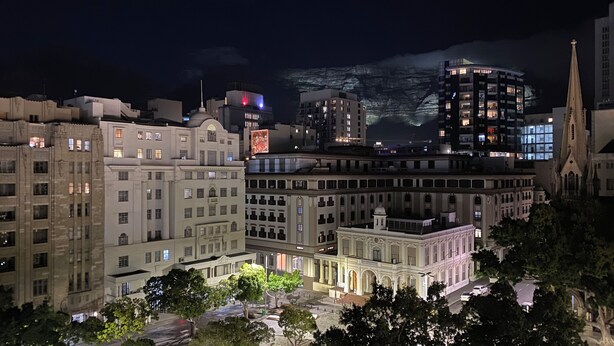 A nighttime cityscape with historic buildings, a prominent church spire, and a modern high-rise with illuminated windows. - Cape Town Urban Elegance on Long Street | Unbeatable Table Mountain View’s (Cape Town)