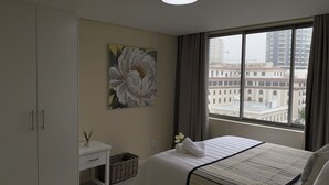 A hotel room with a bed, a nightstand, a painting, a window with a view of buildings, and a wardrobe. - Cape Town Urban Elegance on Long Street | Unbeatable Table Mountain View’s (Cape Town)