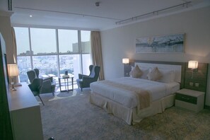 Une chambre d’hôtel avec un grand lit, deux tables de chevet, une chaise, une petite table et une grande fenêtre donnant sur la ville.