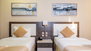 Een hotelkamer met twee bedden, een nachtkastje, een lamp en twee schilderijen aan de muur.