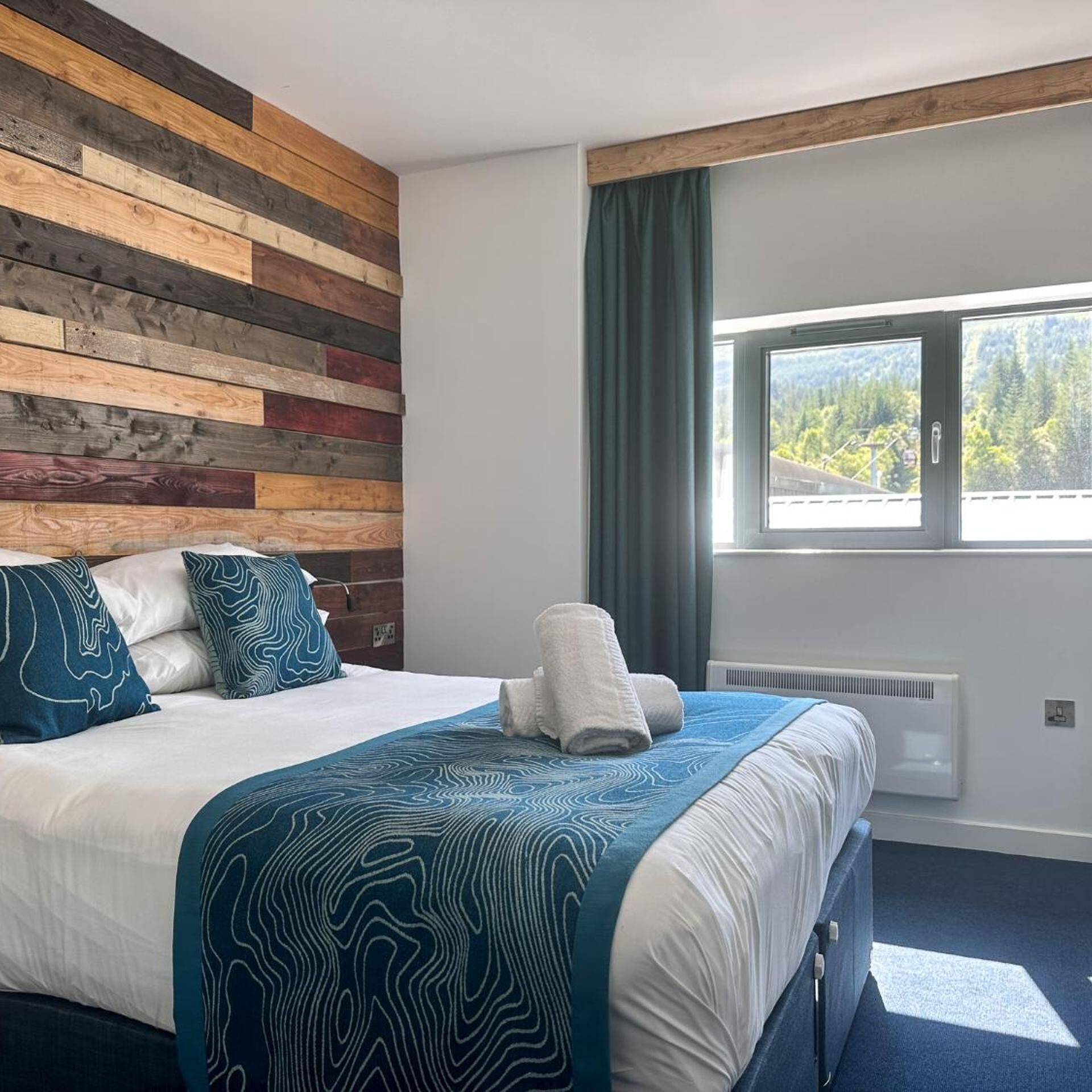Habitación de hotel con cama, un muro decorativo de madera, ventana con vistas y alfombra azul.