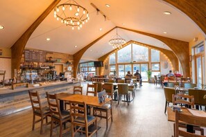 A spacious café with wooden beams, large windows, and a variety of seating arrangements. - The Base Camp Hotel (Fort William)