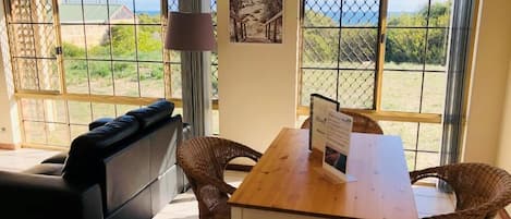 Une pièce comprenant un canapé, une table à manger avec des chaises, une lampe et de grandes fenêtres donnant sur l’extérieur.