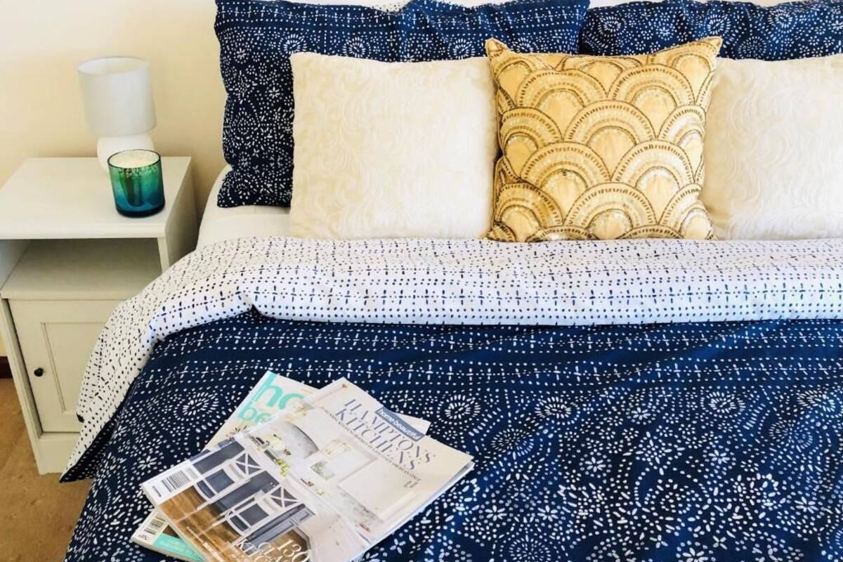 A bed with patterned bedding, a bedside table with a lamp, and a magazine on the bed.