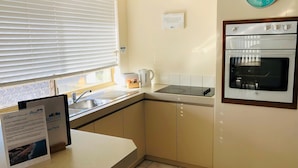 Una cocina con horno empotrado, un reloj y una ventana con persianas.