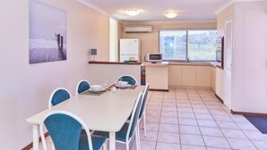 Un comedor con mesa y sillas, una cocina equipada y un ventanal con persianas.