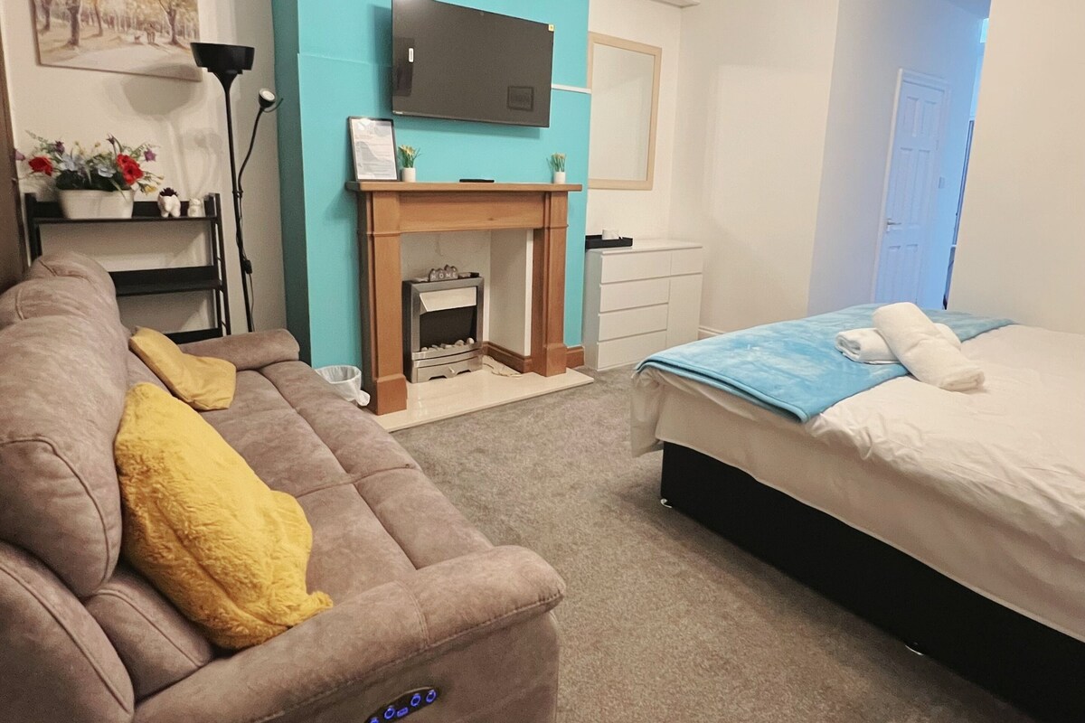 A modern bedroom with a sofa, a bed, a TV, a fireplace, and a hallway.