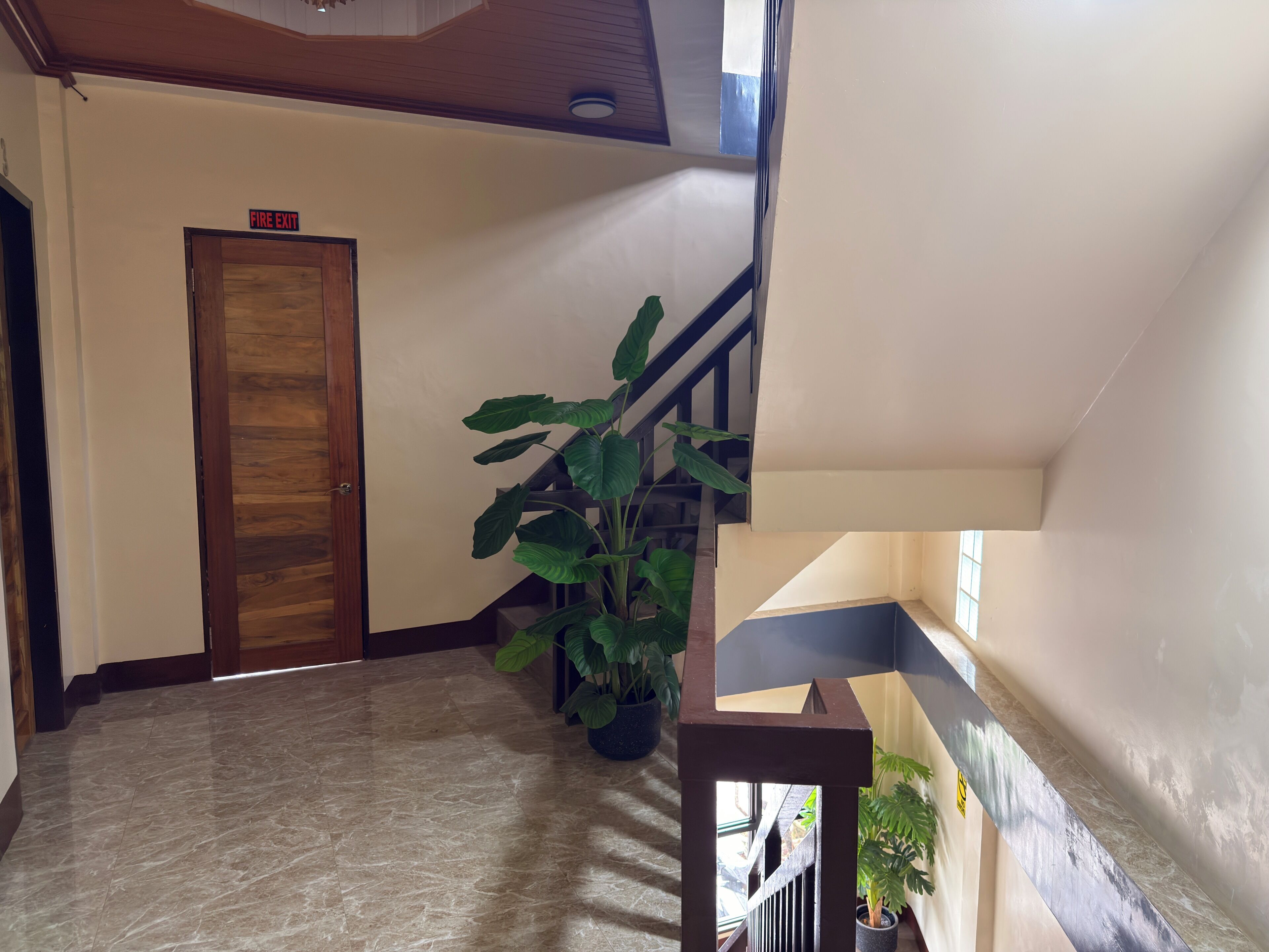 Un pasillo con un letrero de salida de incendios, una escalera y plantas en macetas.