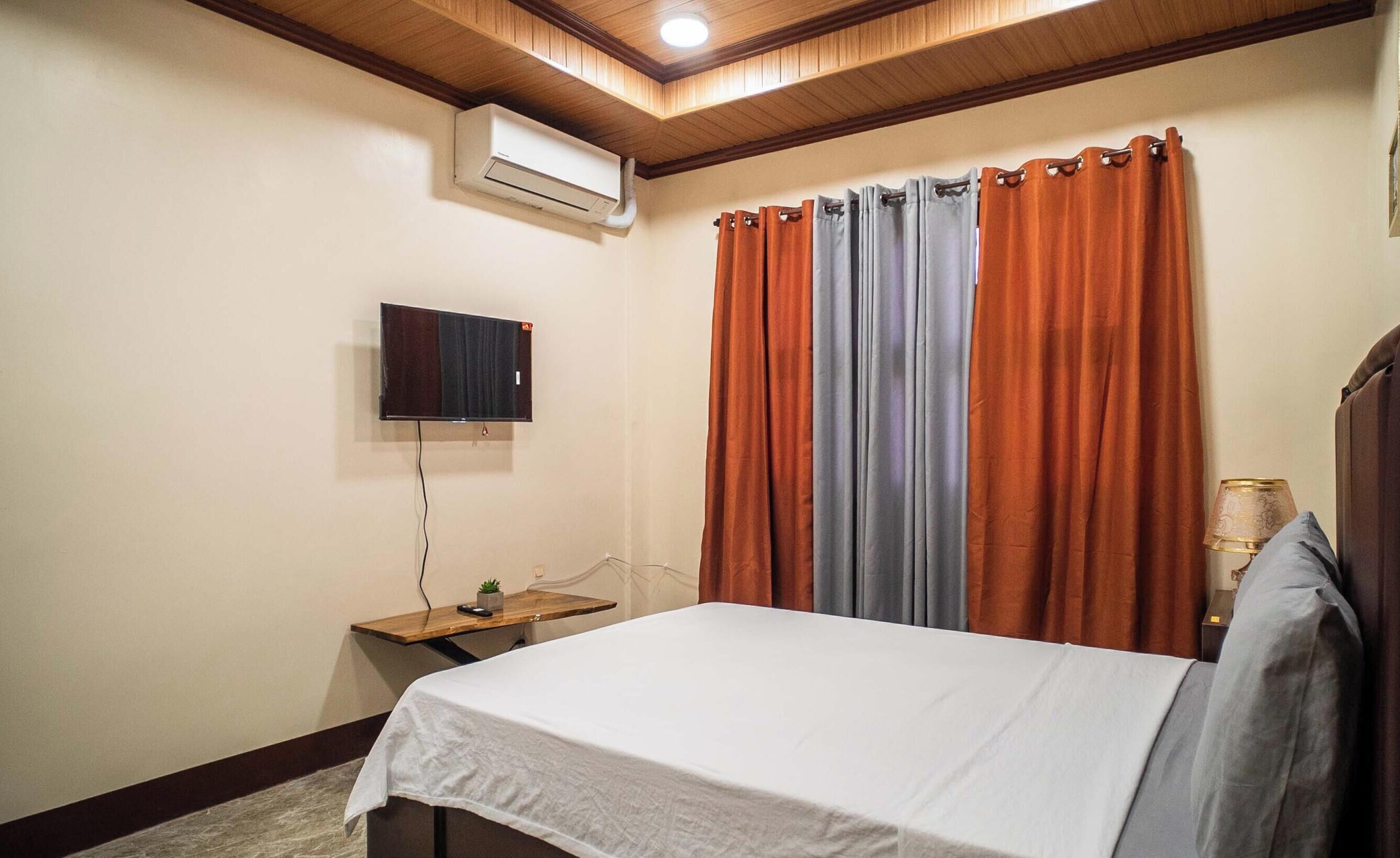 Un dormitorio con una cama, un aire acondicionado, un televisor y cortinas.