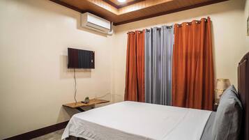 Un dormitorio con una cama, un aire acondicionado, un televisor y cortinas.