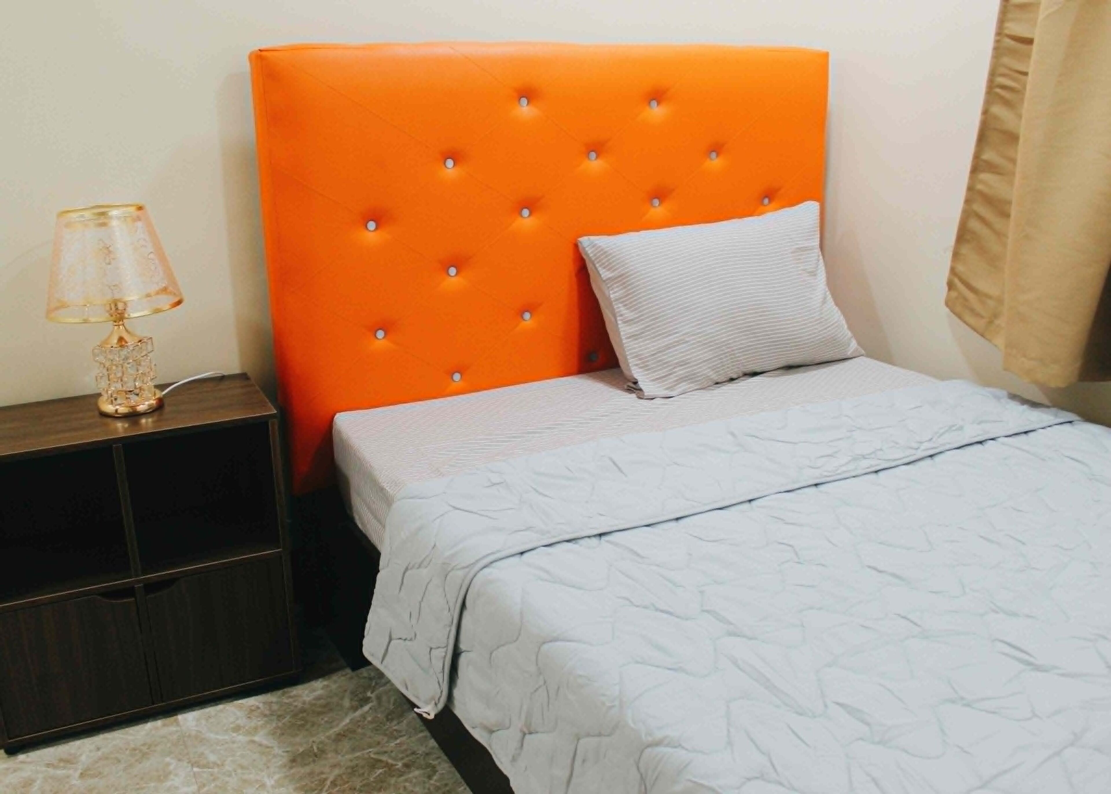 Una cama con cabecera naranja, almohada blanca y cubrecama gris.