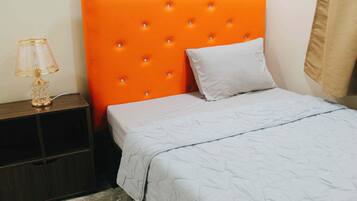 Una cama con cabecera naranja, almohada blanca y cubrecama gris.