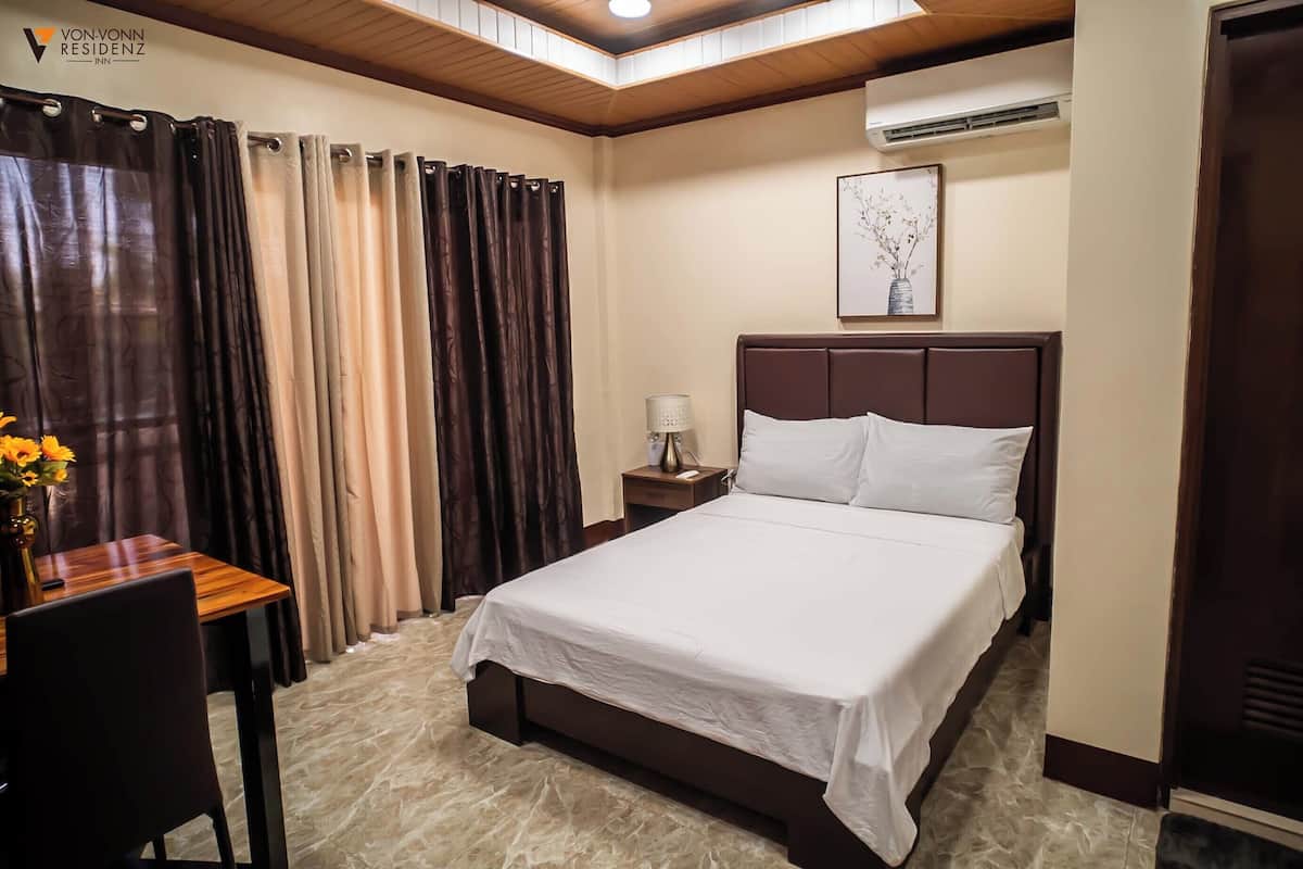 Habitación de hotel con cama, escritorio, silla, mesita de noche, lámpara y un cuadro en la pared.