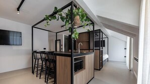 A modern kitchen with a central island, bar stools, and a hanging plant. - Hortenberg Homes (Bolzano)