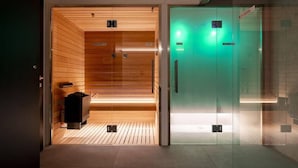 A sauna room with wooden walls and a bench, and a glass elevator with a green light. - Hortenberg Homes (Bolzano)