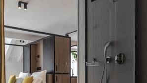 A modern hotel room with a glass partition, a shower, and a bed with white and yellow pillows. - Hortenberg Homes (Bolzano)