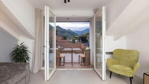 A room with a sliding glass door leading to a balcony with a table and chairs, a sofa, and a chair. - Hortenberg Homes (Bolzano)