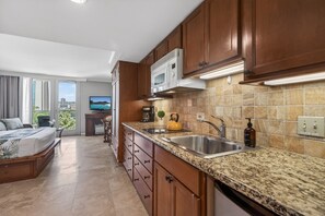 A modern kitchen with granite countertops, wooden cabinets, a built-in microwave, and a large window offering a city view. - Island Retreat at the Luana Waikiki (Honolulu)