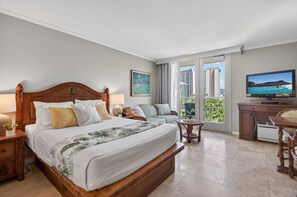 A hotel room with a large bed, a television, a sofa, a small table, and a balcony with a city view. - Island Retreat at the Luana Waikiki (Honolulu)