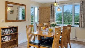 Un coin repas avec une table et des chaises en bois, une bibliothèque et une vue dégagée grâce à de grandes fenêtres.