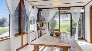 Une véranda avec une table en bois, des rideaux blancs et une vue sur un paysage verdoyant.