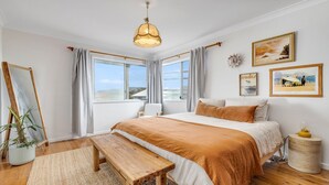 Une chambre avec un grand lit, un banc en bois, un luminaire suspendu et une fenêtre avec des rideaux.