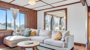 A living room with a sofa, a round coffee table, and large windows with curtains. - Heaven's @ Crescent Head (Crescent Head)