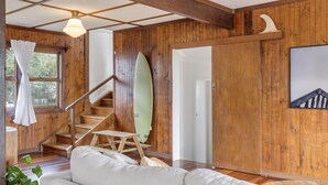 Un intérieur en bois avec un escalier, une planche de surf, un canapé blanc et un tableau encadré au mur.