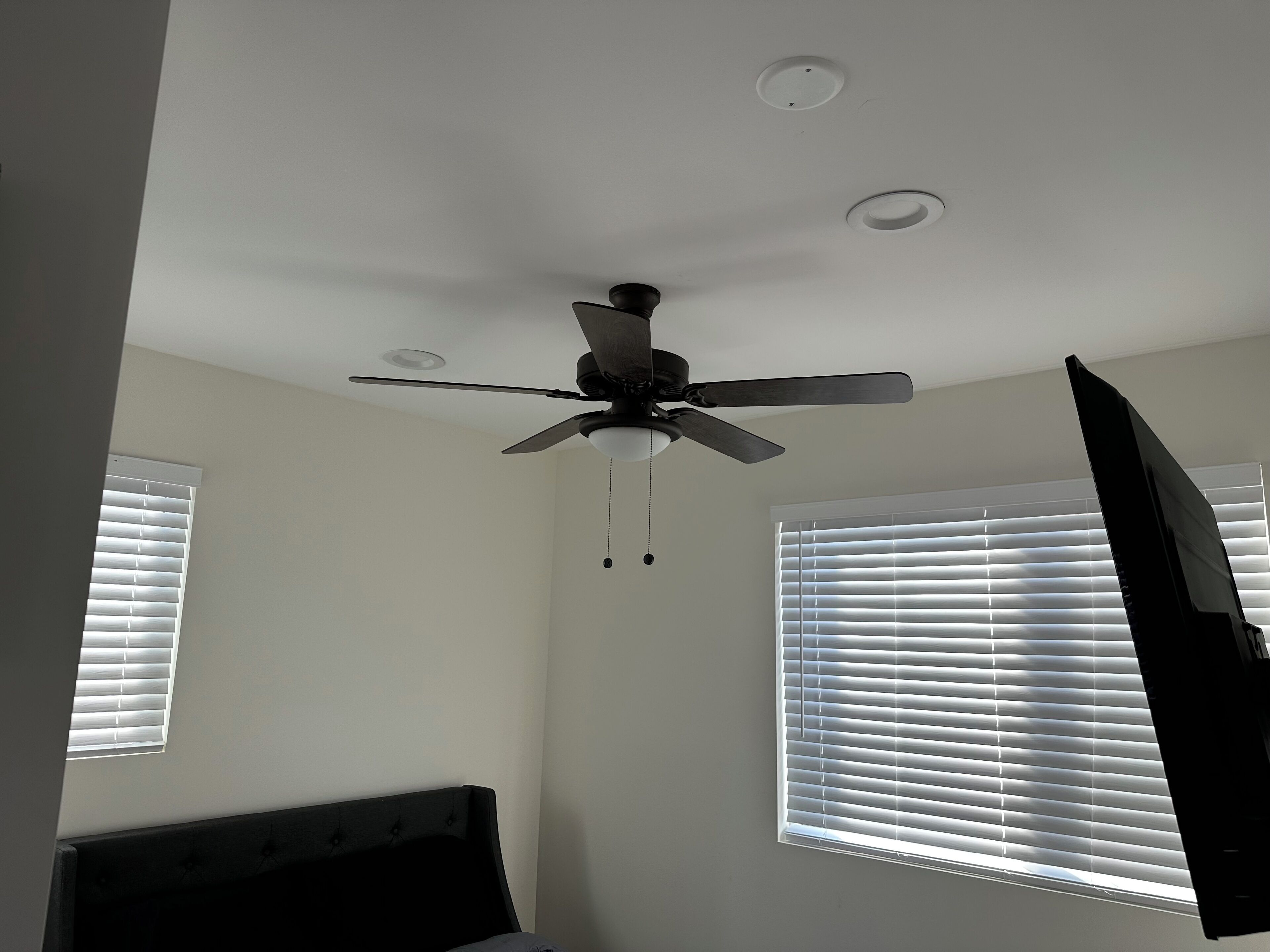 Una camera da letto con un ventilatore a soffitto, due finestre con persiane e un letto.