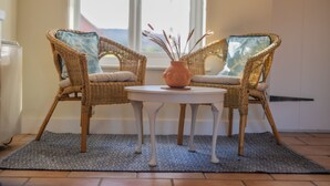 Ein Zimmer mit zwei Korbstühlen, einem kleinen weißen Tisch und einer Vase mit Trockenpflanzen.