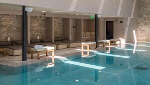 Ein Schwimmbecken mit Liegestühlen und Tischen, eine Steinmauer sowie eine Decke mit Einbuchtungslampen.