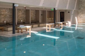 Ein Schwimmbecken mit Liegestühlen und Tischen, eine Steinmauer sowie eine Decke mit Einbuchtungslampen.