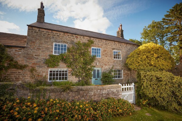 A stone building with a gabled roof, multiple windows, and a white picket fence. - High Swinton Cottage (Ripon)