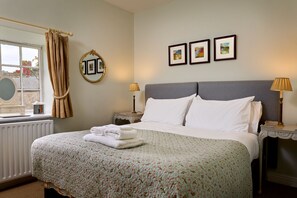 A neatly made bed with a floral bedspread, a round mirror, and two bedside lamps. - High Swinton Cottage (Ripon)