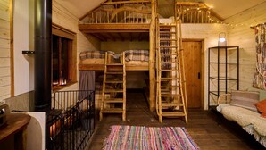 A cozy cabin with a loft bedroom, a wooden ladder, a fireplace, and a cozy seating area.