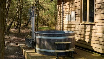 A rustic cabin with a hot tub, a chimney, and a wooden deck.