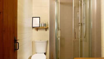 A bathroom with a toilet, a shower enclosure, and a wooden shelf with toiletries.