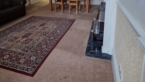 A living room with a dark-colored sofa, a patterned rug, a dining table with chairs, and a fireplace. - Spacious Clean Central Near Train Stn & University (Edinburgh)