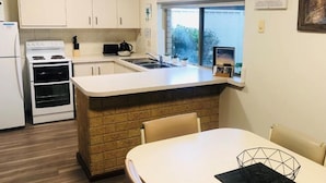 A kitchen with white cabinets, a stove, a sink, and a window. - Apiwa Busselton Seaside Escape Apartments (Busselton)