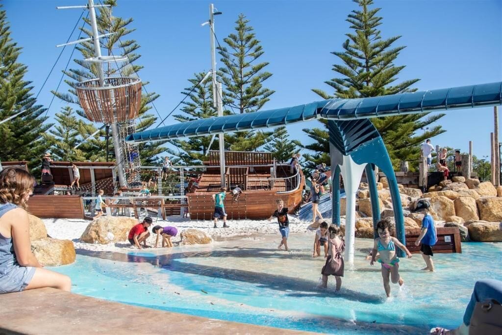 A water park with a ship-themed play area, a pool, and surrounding trees.