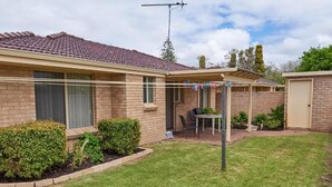 A residential house with a tiled roof, a covered patio with a table and chairs, and a small garden area. - Apiwa Busselton Seaside Escape Apartments (Busselton)