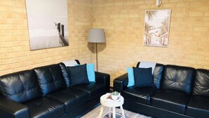A room with two black leather sofas, a small white side table, and a lamp. - Apiwa Busselton Seaside Escape Apartments (Busselton)