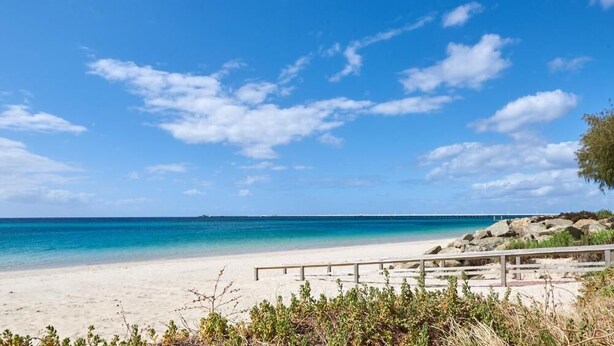 A beach with clear blue water, a sandy shore, and a wooden walkway. - Apiwa Busselton Seaside Escape Apartments (Busselton)