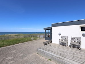 A coastal property with a wooden deck, a glass door leading to a room, and a view of the sea. - 4 Star Holiday Home in Lokken (Lokken)