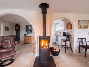 A living room with a fireplace, wooden flooring, a leather chair, and an arched doorway leading to a kitchen. - 4 Star Holiday Home in Lokken (Lokken)