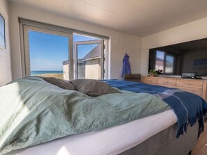A bedroom with a bed, a television, a dresser, and a view of the beach. - 4 Star Holiday Home in Lokken (Lokken)