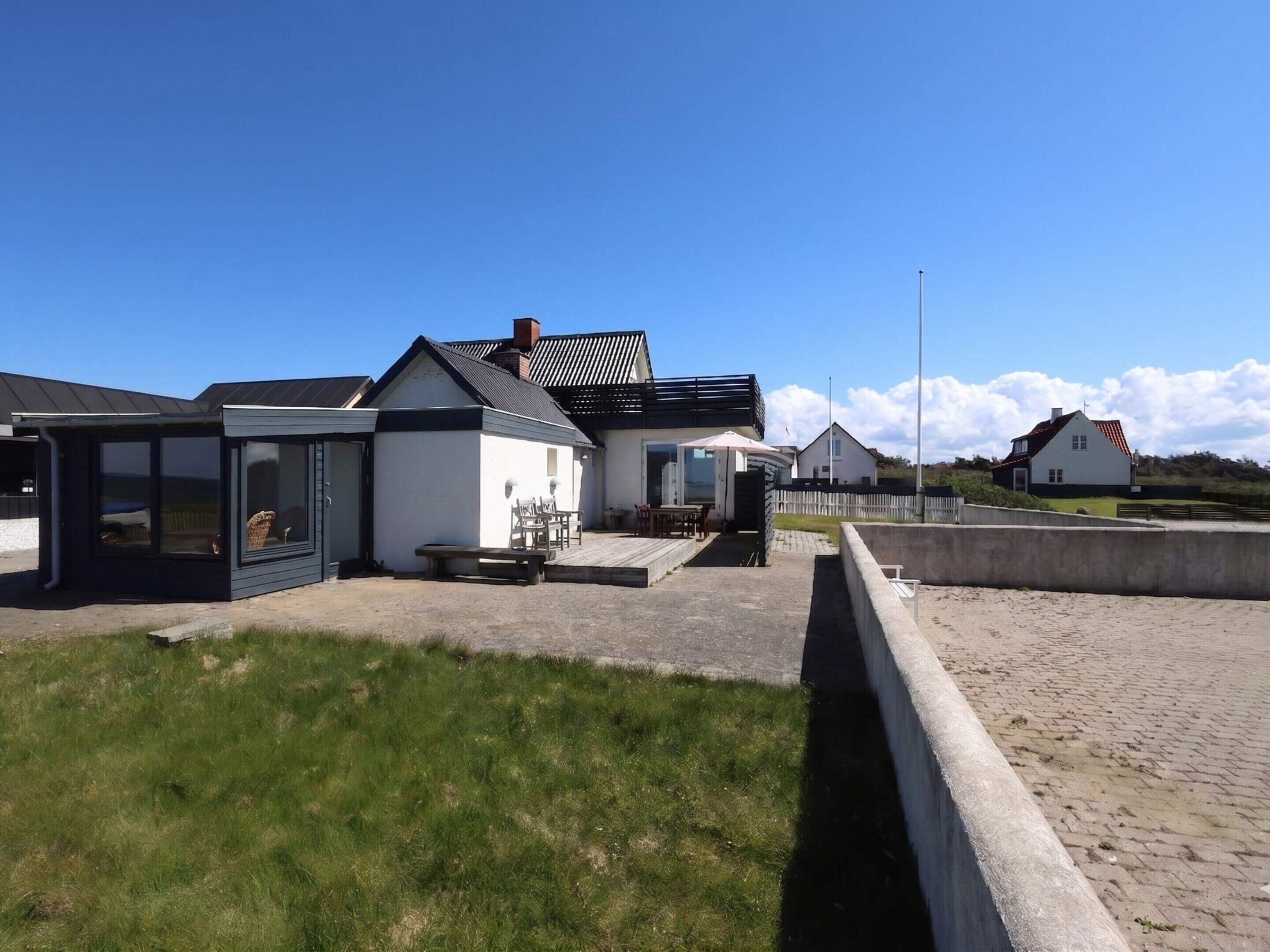 A coastal building with a covered patio, a small outdoor seating area, and a view of the sea.