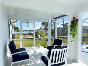 Eine überdachte Terrasse mit weißer Möbel, einer hängenden Pflanze und Blick auf einen Rasen und Häuser.